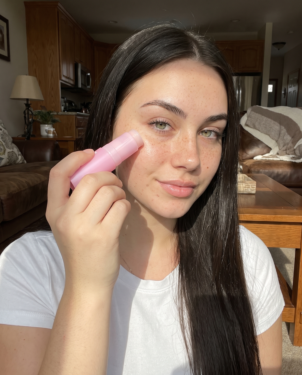 Woman holding a balm stick by a window in soft daylight