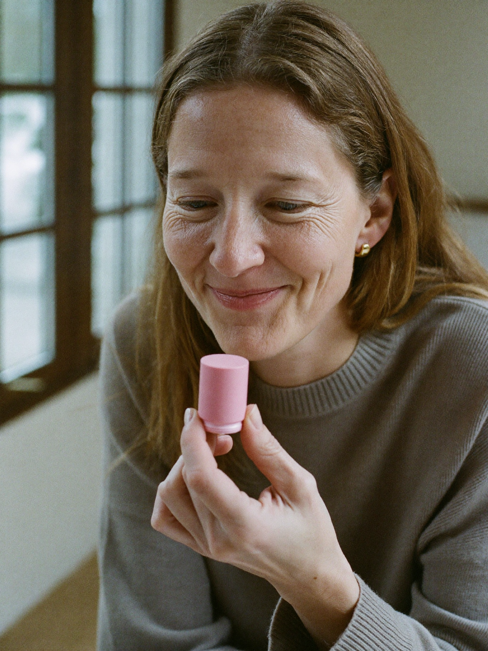 Woman holding a balm stick by a window in soft daylight